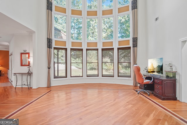 home office with ornamental molding, a high ceiling, and light wood-type flooring