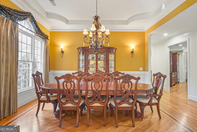 dining space with a notable chandelier, a raised ceiling, ornamental molding, and light hardwood / wood-style flooring