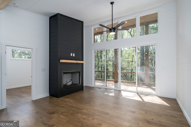 unfurnished living room with ceiling fan, plenty of natural light, a high ceiling, and dark hardwood / wood-style flooring