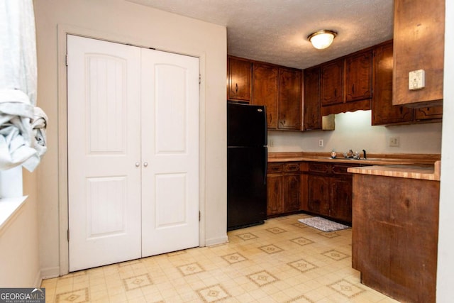 kitchen with butcher block counters, sink, black refrigerator, and a textured ceiling