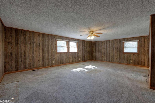 unfurnished room with ceiling fan, carpet floors, wooden walls, and plenty of natural light