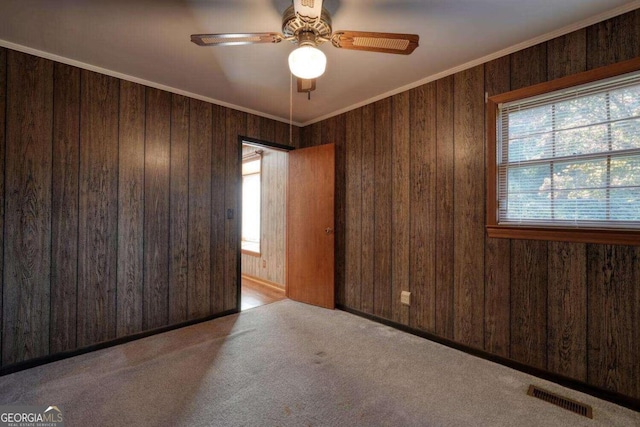 spare room with light carpet, crown molding, ceiling fan, and wooden walls