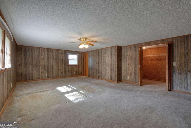 carpeted spare room with a textured ceiling, wooden walls, and ceiling fan