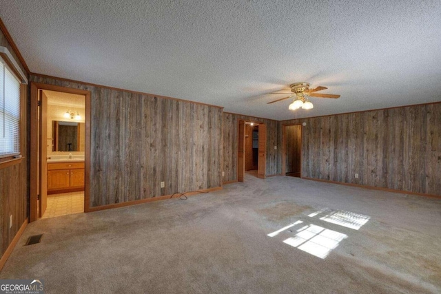 empty room with a textured ceiling, light colored carpet, wooden walls, and ceiling fan