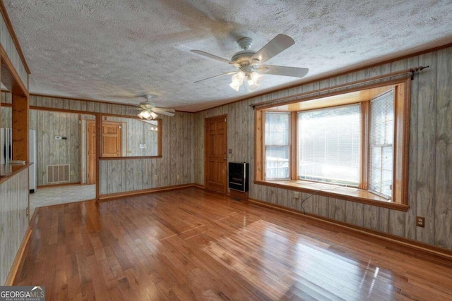 unfurnished living room with light wood-type flooring, wooden walls, ceiling fan, and a textured ceiling