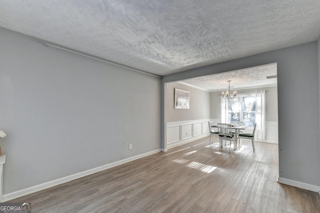 unfurnished dining area featuring wood-type flooring, an inviting chandelier, and a textured ceiling