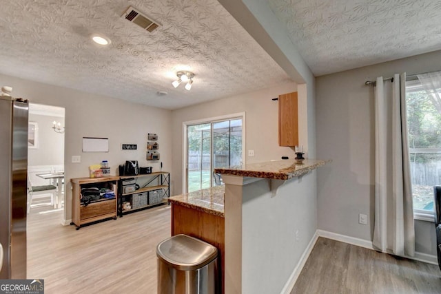 kitchen featuring stainless steel fridge, kitchen peninsula, a breakfast bar area, light hardwood / wood-style flooring, and a textured ceiling