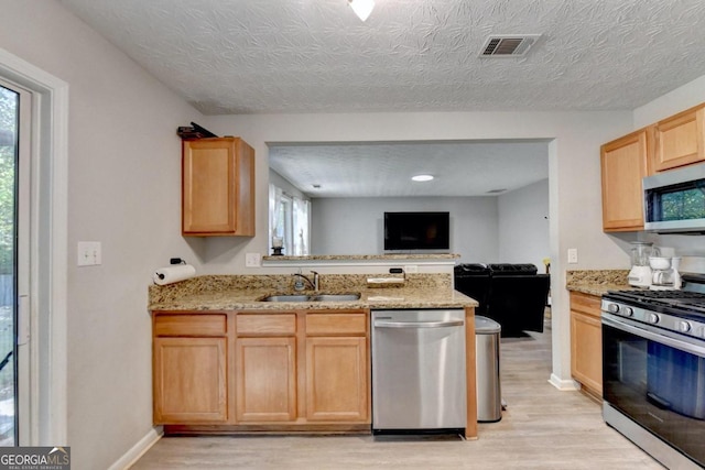 kitchen featuring light wood-type flooring, light brown cabinets, sink, appliances with stainless steel finishes, and a textured ceiling