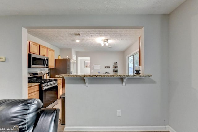 kitchen with light stone counters, kitchen peninsula, a textured ceiling, appliances with stainless steel finishes, and a kitchen breakfast bar