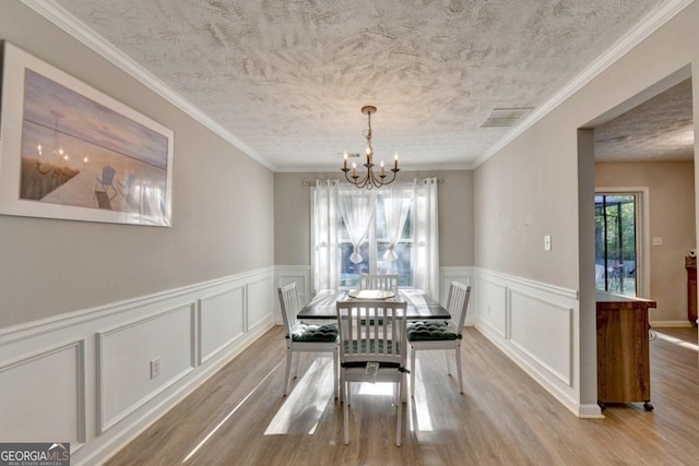 dining area featuring light hardwood / wood-style floors, a chandelier, ornamental molding, and a textured ceiling