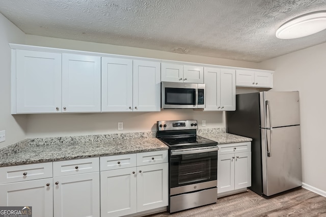 kitchen featuring light wood-type flooring, light stone counters, white cabinets, appliances with stainless steel finishes, and a textured ceiling