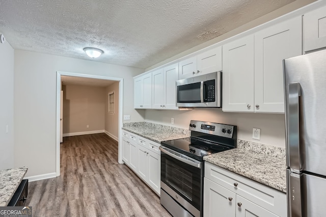 kitchen featuring light stone counters, white cabinets, appliances with stainless steel finishes, and light hardwood / wood-style floors