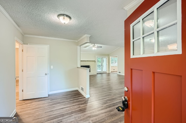 entrance foyer featuring a brick fireplace, ceiling fan, hardwood / wood-style flooring, crown molding, and a textured ceiling