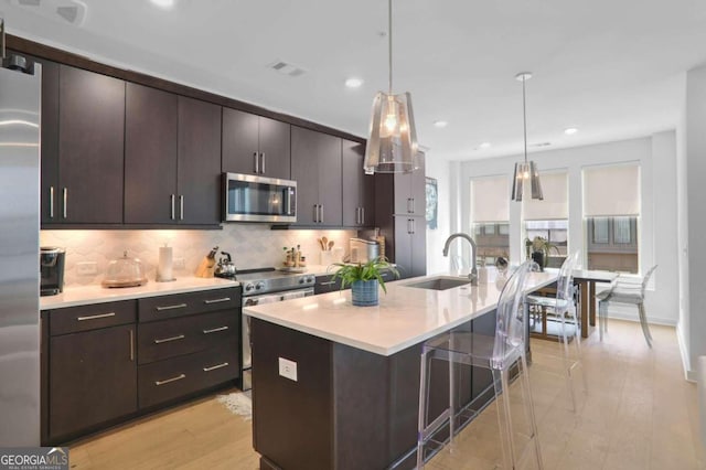 kitchen featuring dark brown cabinetry, sink, an island with sink, decorative light fixtures, and appliances with stainless steel finishes