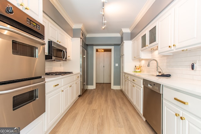 kitchen with light wood-type flooring, decorative backsplash, ornamental molding, white cabinetry, and appliances with stainless steel finishes