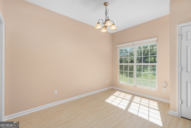 empty room with a notable chandelier, light hardwood / wood-style flooring, and a textured ceiling