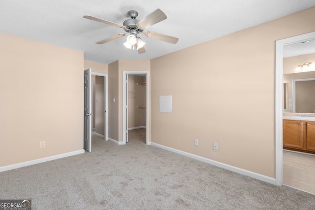 unfurnished bedroom with a spacious closet, light carpet, ensuite bathroom, and ceiling fan