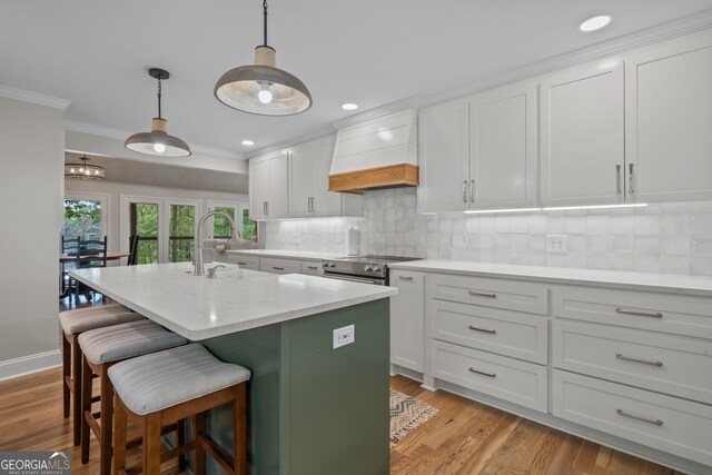 kitchen with an island with sink, sink, light wood-type flooring, and white cabinetry