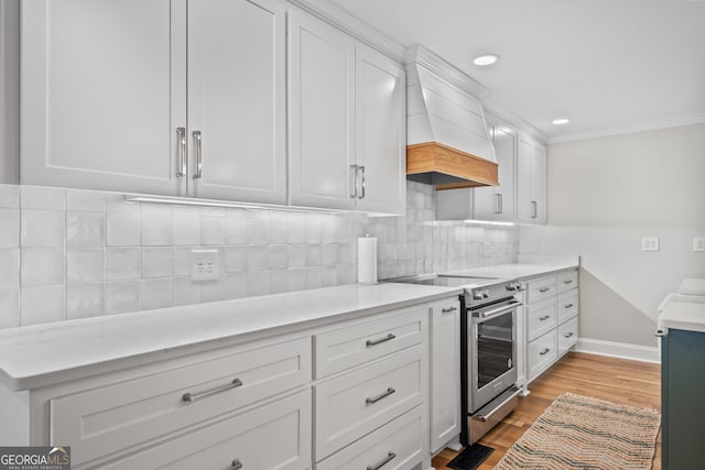 kitchen featuring light wood-type flooring, tasteful backsplash, white cabinetry, custom exhaust hood, and stainless steel electric range