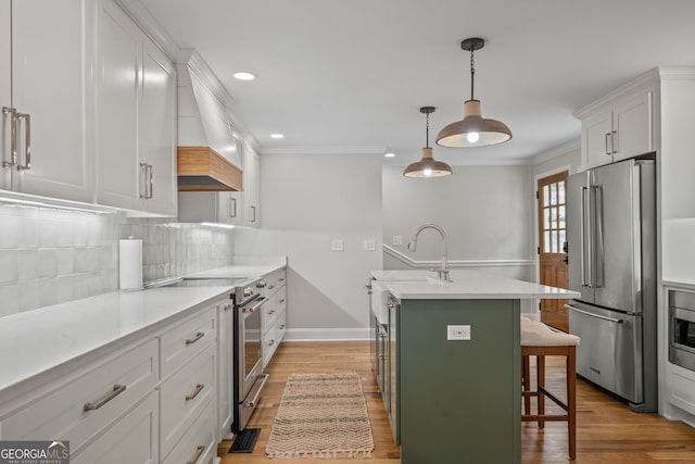 kitchen featuring custom range hood, white cabinets, sink, premium appliances, and a breakfast bar area