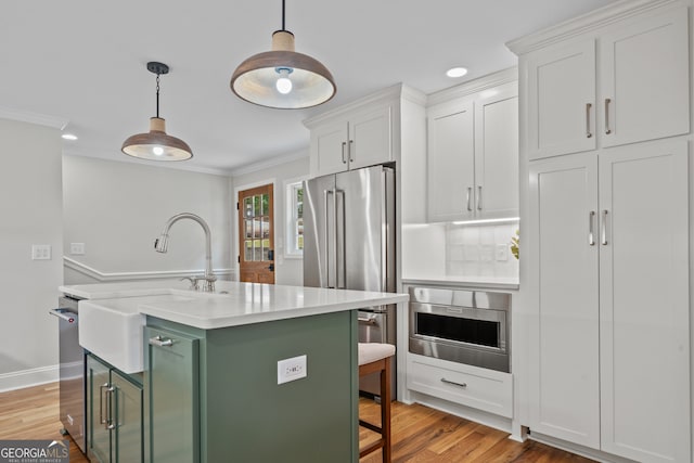 kitchen featuring pendant lighting, a center island with sink, stainless steel appliances, white cabinets, and a kitchen bar