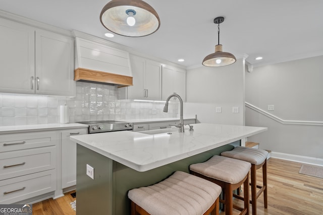 kitchen featuring tasteful backsplash, light hardwood / wood-style flooring, stainless steel stove, a center island with sink, and custom exhaust hood