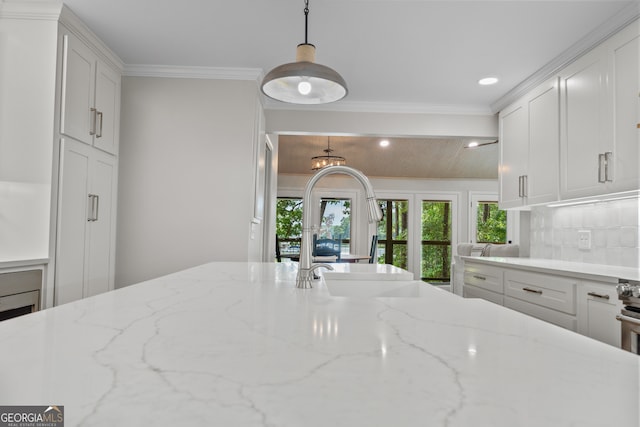 kitchen with light stone countertops, tasteful backsplash, white cabinets, sink, and decorative light fixtures