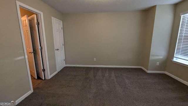 spare room with dark colored carpet, a textured ceiling, and a healthy amount of sunlight