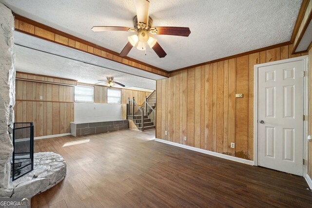 interior space with ceiling fan, a textured ceiling, wood walls, dark hardwood / wood-style floors, and a fireplace