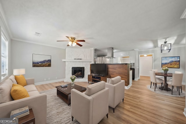 living room with a large fireplace, ornamental molding, light wood-type flooring, and ceiling fan