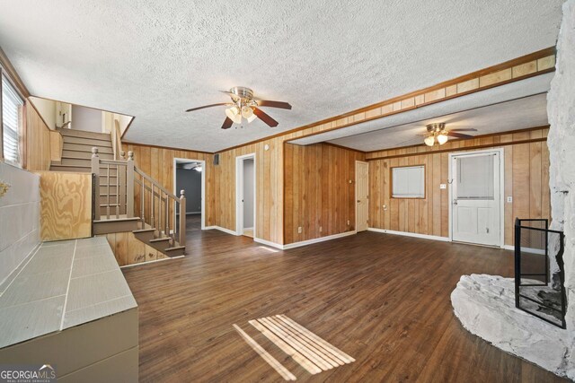 unfurnished living room featuring wood walls, a textured ceiling, and dark hardwood / wood-style flooring