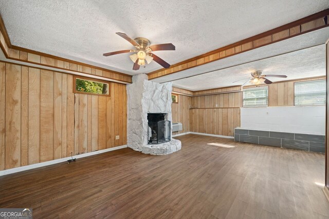 unfurnished living room with ceiling fan, a textured ceiling, dark hardwood / wood-style floors, a fireplace, and wooden walls