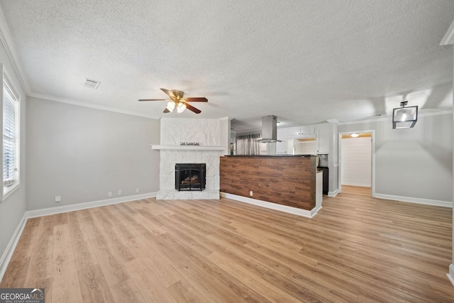 unfurnished living room featuring crown molding, a textured ceiling, light wood-type flooring, and ceiling fan