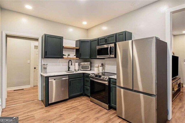 kitchen with light stone counters, tasteful backsplash, sink, light hardwood / wood-style flooring, and appliances with stainless steel finishes