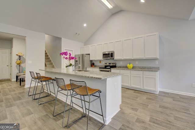 kitchen featuring light wood-type flooring, light stone countertops, white cabinets, a breakfast bar area, and appliances with stainless steel finishes