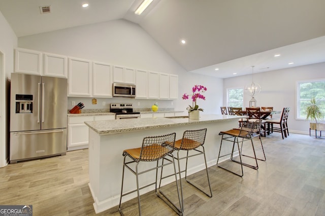 kitchen with stainless steel appliances, white cabinets, a center island with sink, and a healthy amount of sunlight