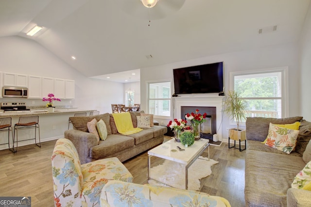 living room with lofted ceiling, ceiling fan, and light hardwood / wood-style flooring