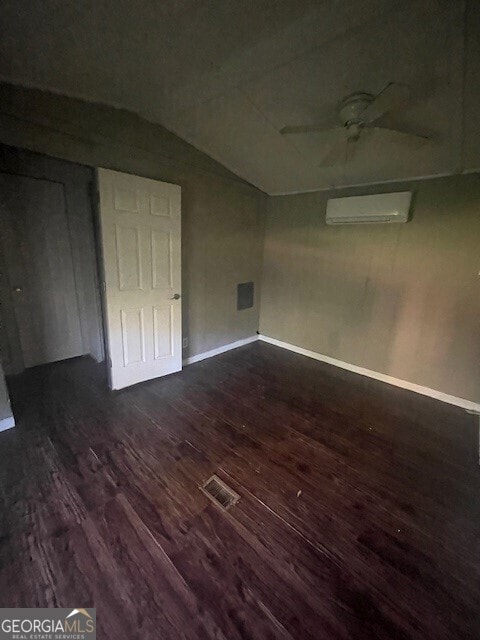 spare room featuring an AC wall unit, ceiling fan, and dark wood-type flooring