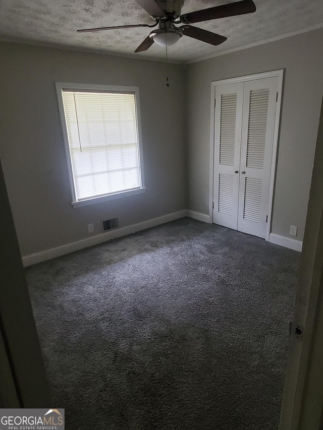 unfurnished bedroom with a textured ceiling, a closet, dark carpet, and ceiling fan