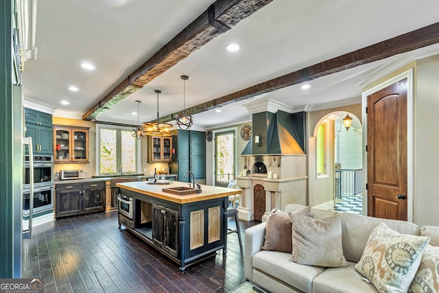 kitchen featuring a kitchen island with sink, dark hardwood / wood-style floors, beam ceiling, wall chimney exhaust hood, and sink