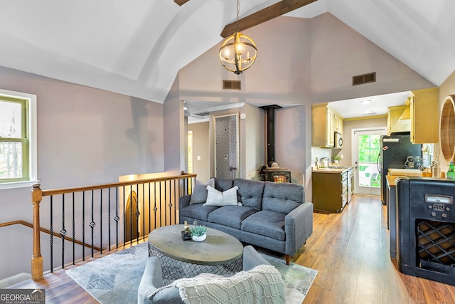 living room with an inviting chandelier, light hardwood / wood-style flooring, high vaulted ceiling, and a wood stove