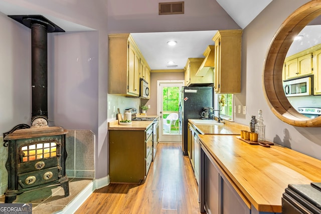 kitchen with range with electric cooktop, butcher block countertops, light hardwood / wood-style flooring, and a wood stove