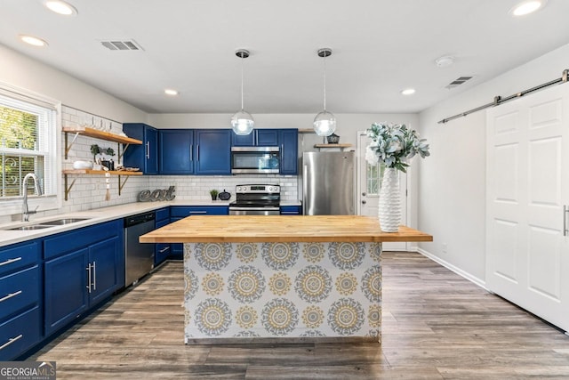 kitchen with blue cabinetry, butcher block counters, sink, a barn door, and appliances with stainless steel finishes