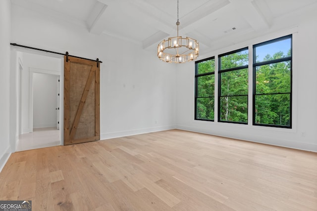 spare room with beamed ceiling, coffered ceiling, a barn door, and light hardwood / wood-style flooring