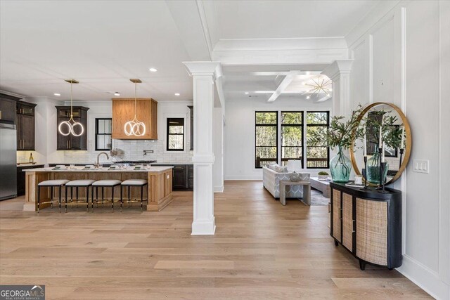 kitchen featuring sink, tasteful backsplash, a kitchen island with sink, stainless steel appliances, and light wood-type flooring