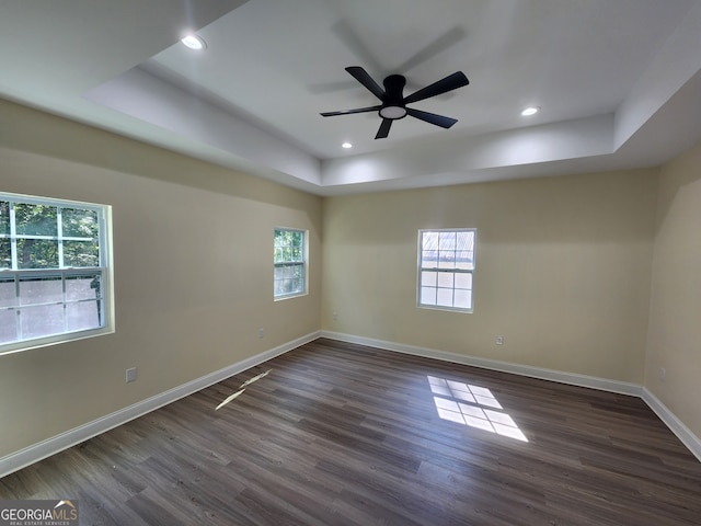 unfurnished room with a healthy amount of sunlight, ceiling fan, dark wood-type flooring, and a raised ceiling