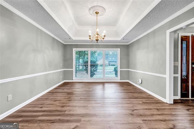 spare room featuring wood-type flooring, an inviting chandelier, a tray ceiling, and ornamental molding