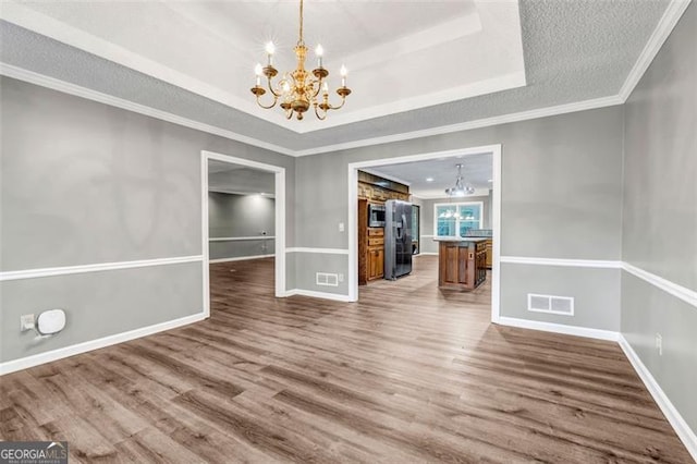 unfurnished dining area with ornamental molding, hardwood / wood-style flooring, a raised ceiling, and a chandelier