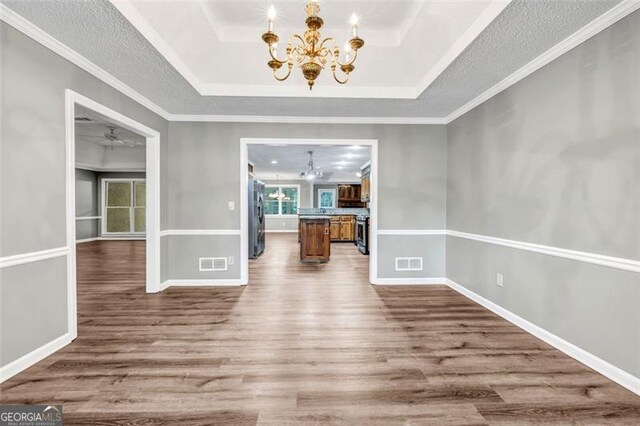 unfurnished dining area featuring wood-type flooring, ornamental molding, a tray ceiling, and a chandelier