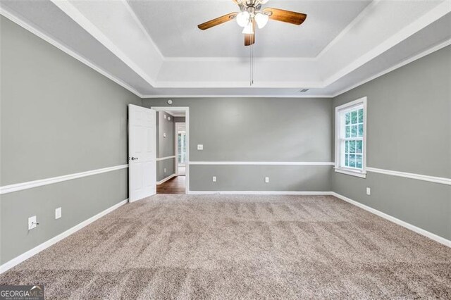 unfurnished bedroom with ceiling fan, a tray ceiling, ornamental molding, and carpet